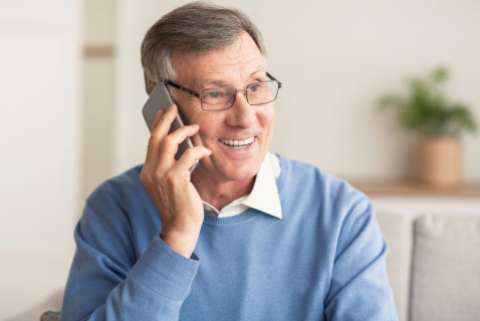 Elderly Man Talking On Cellphone Sitting On Couch At Home