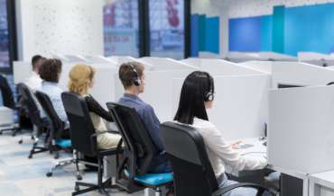 Call center operators sitting in their cubicles, wearing headsets, depicted from behind